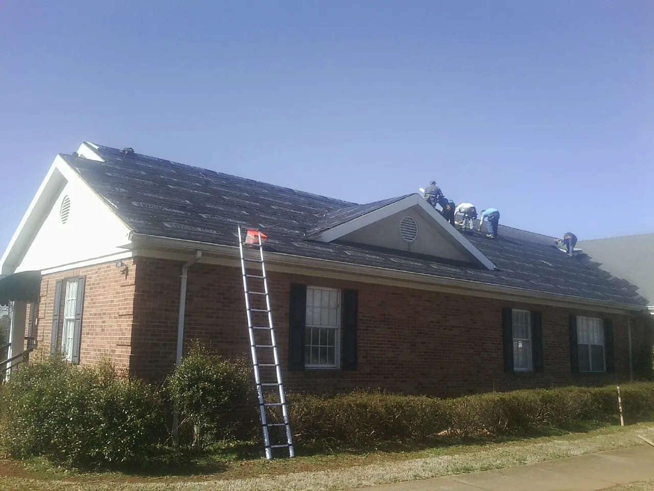 Crew tearing shingles off a brick ranch roof with a ladder set — Metal Roof Repair work by our crew in Basking Ridge
