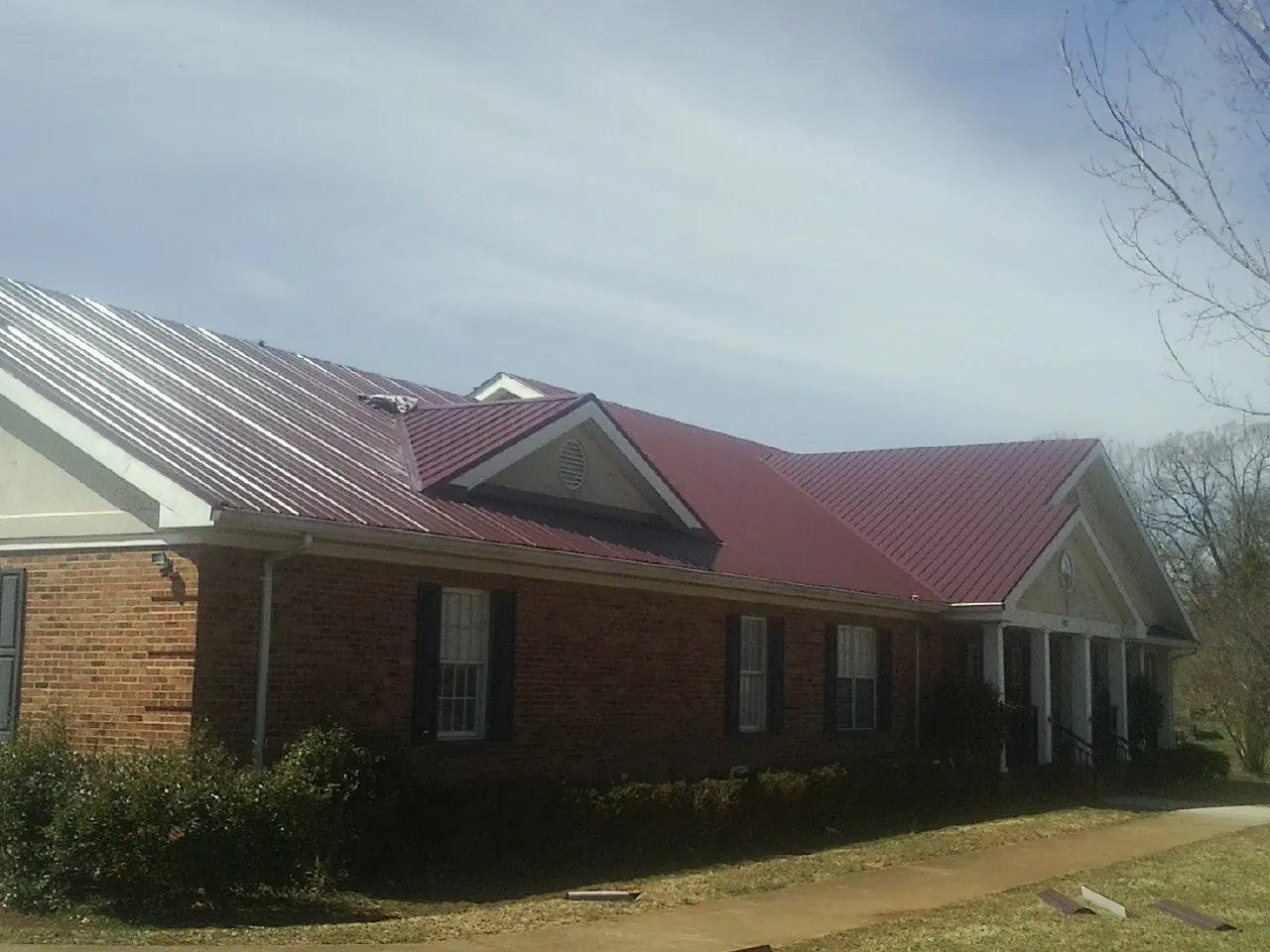 Red metal roof with gabled entries on a long brick building, from a Hail Damage Roof Repair job in Basking Ridge