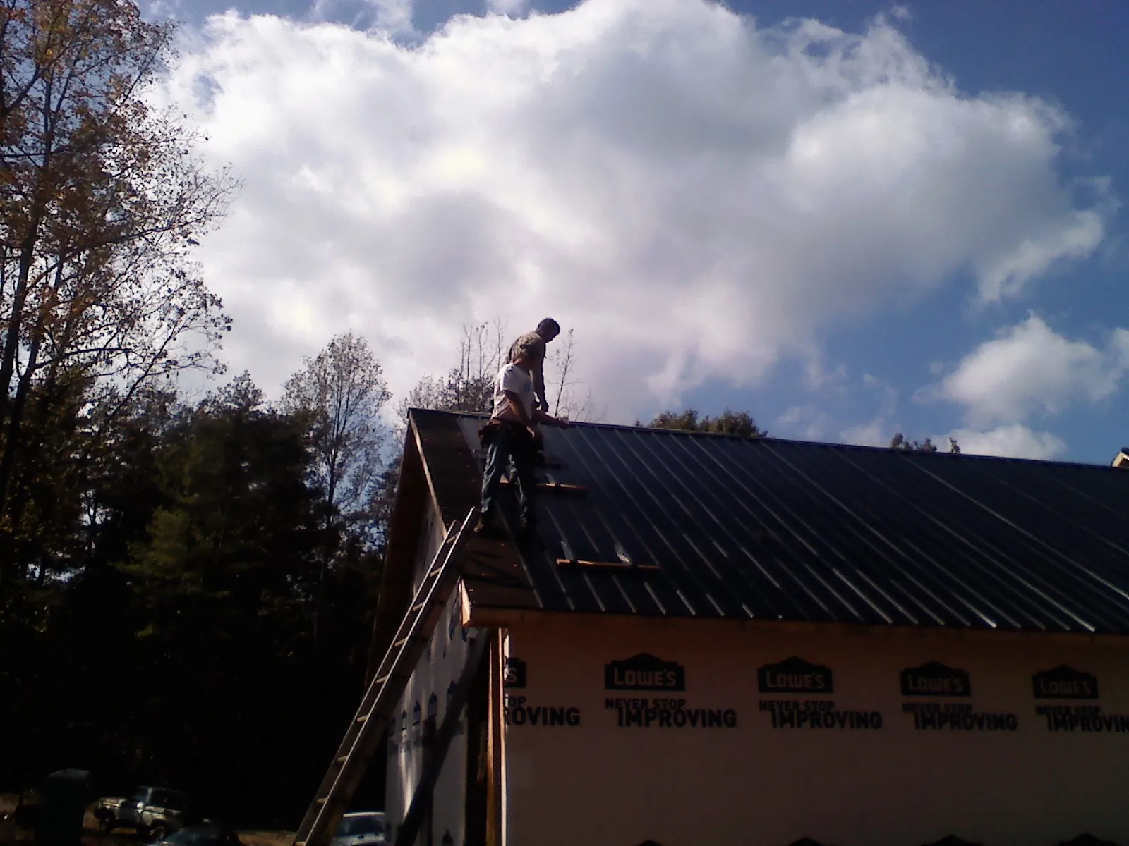Roofer fastening dark metal panels high against a cloudy sky, from a Roof Inspection job in Basking Ridge
